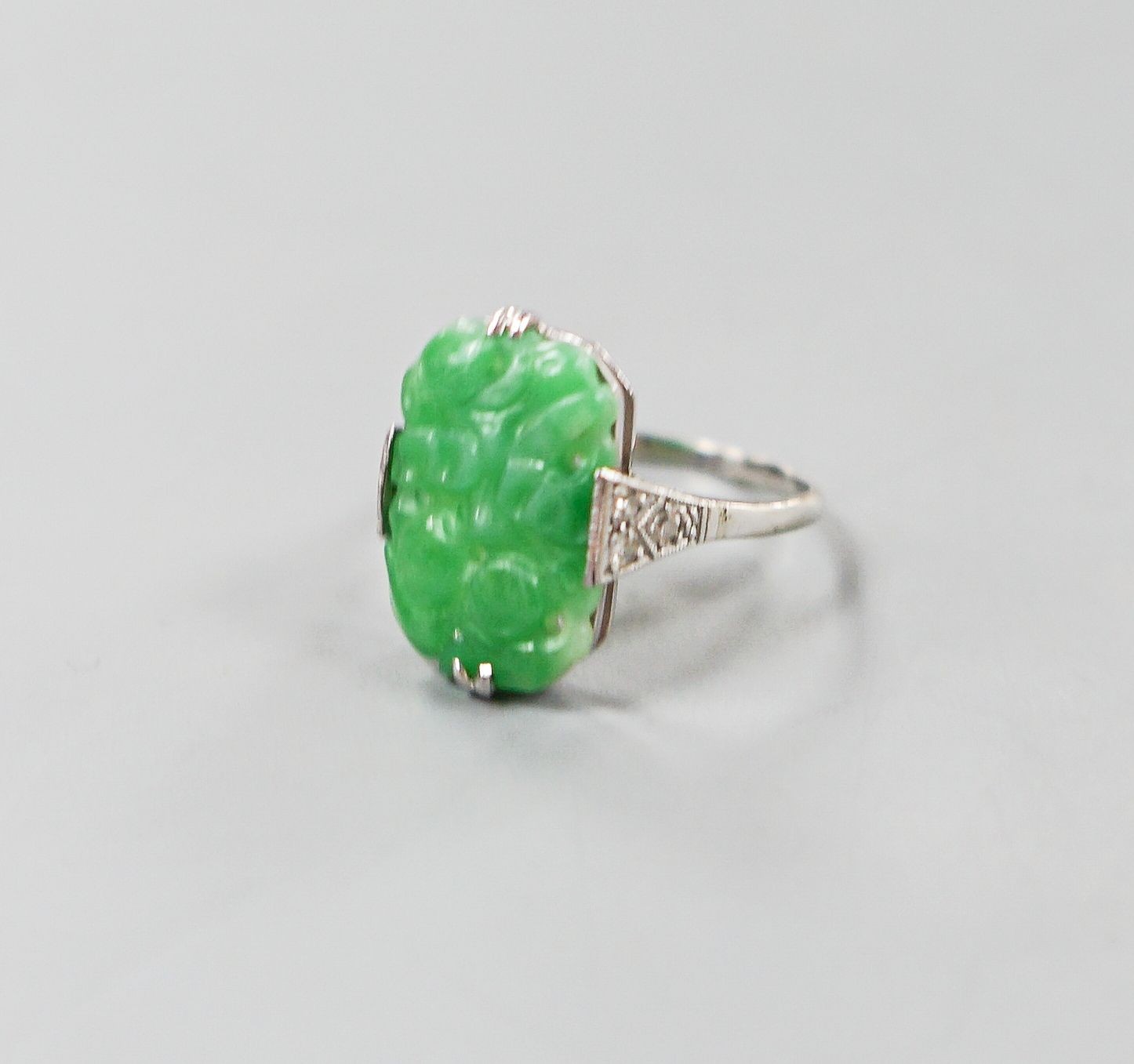 A 1920's 18ct, plat and carved jadeite oval dress ring, size O, gross weight 3.8 grams.